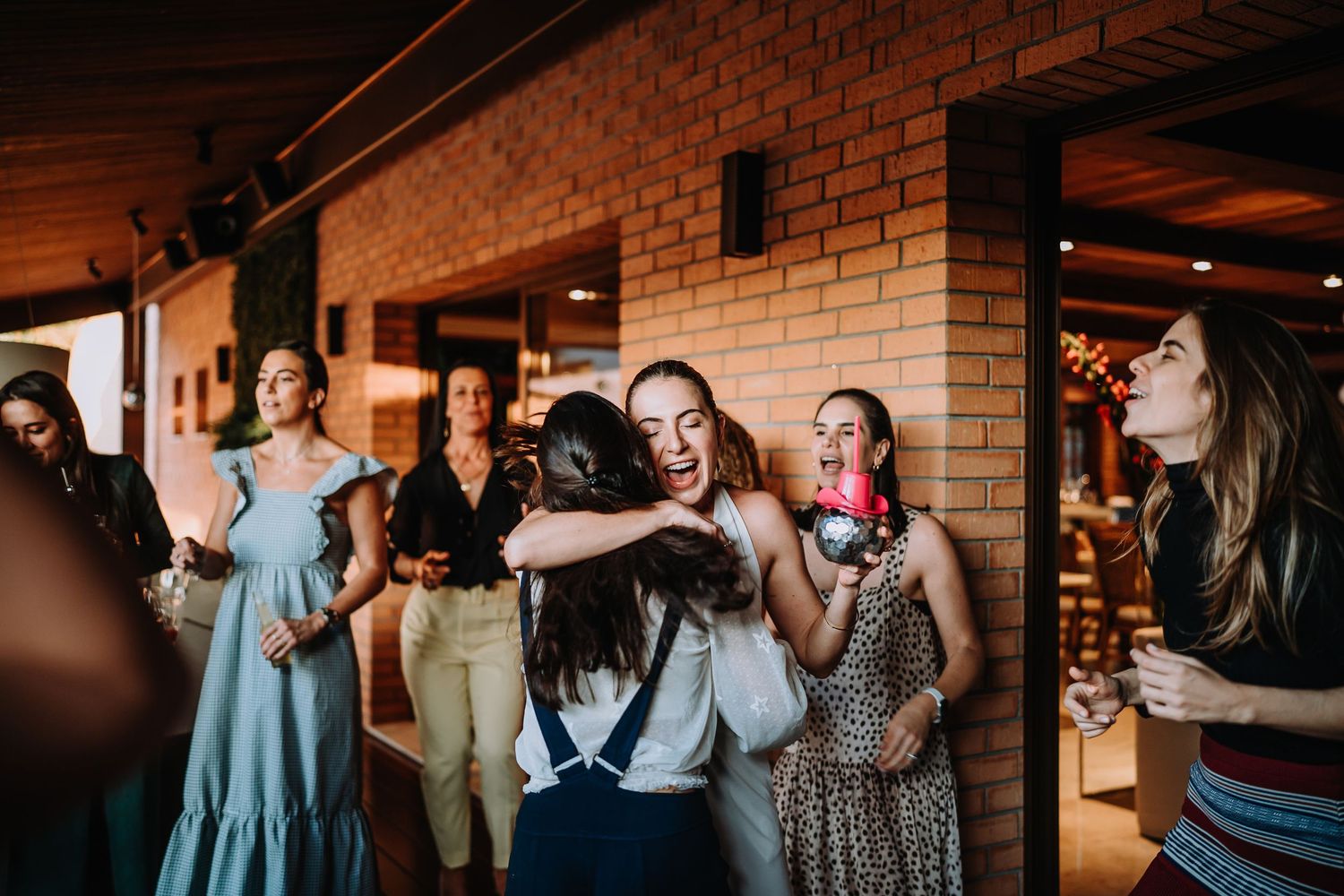 Party guests dance and celebrate in a brick-walled venue with wooden beams.