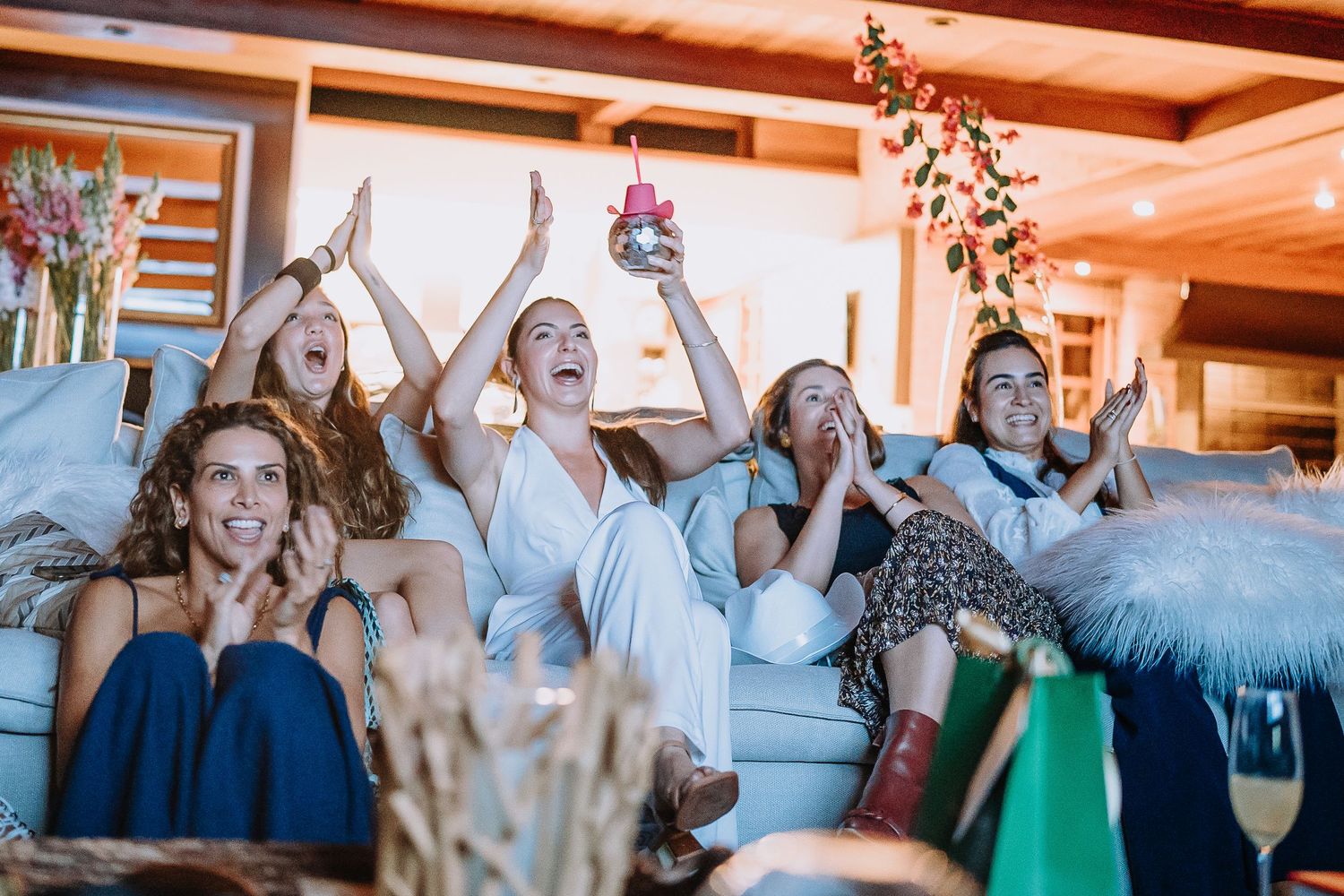 A joyful gathering of friends lounging on a couch with drinks and celebratory expressions.