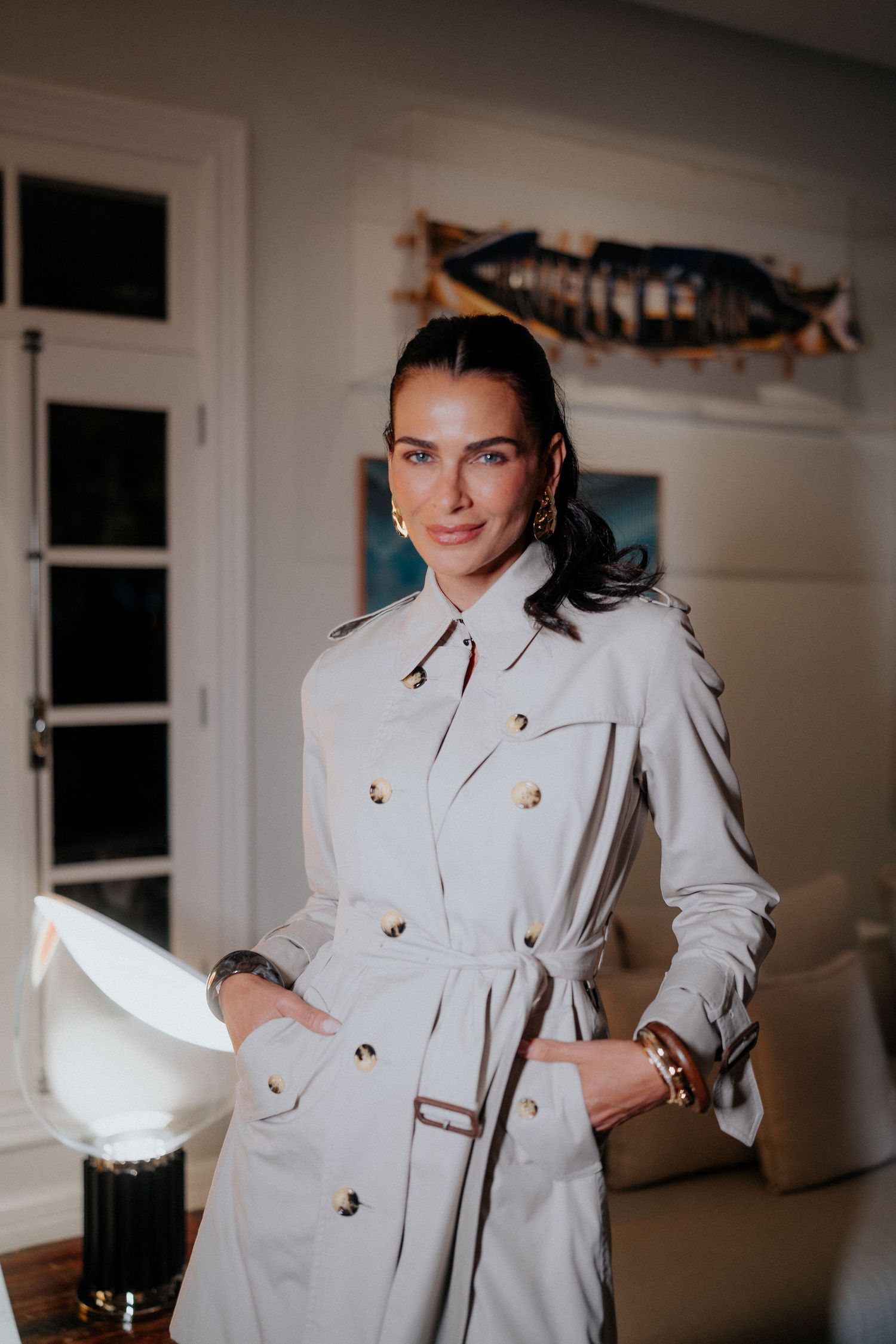 Fashion model posing in elegant white trench coat with gold buttons against neutral interior.
