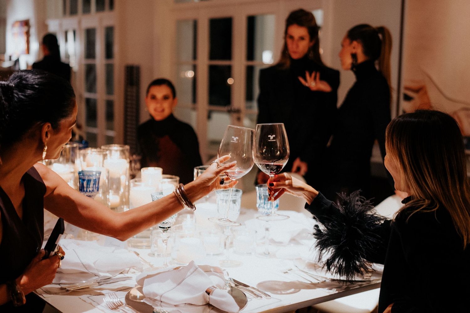 Friends toasting wine glasses around an elegantly set dinner table with candlelight.