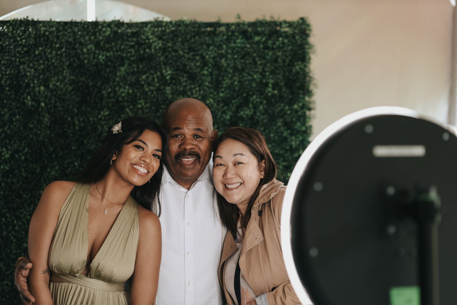 Happy people hugging and posing together in front of verdant greenery backdrop at an event.