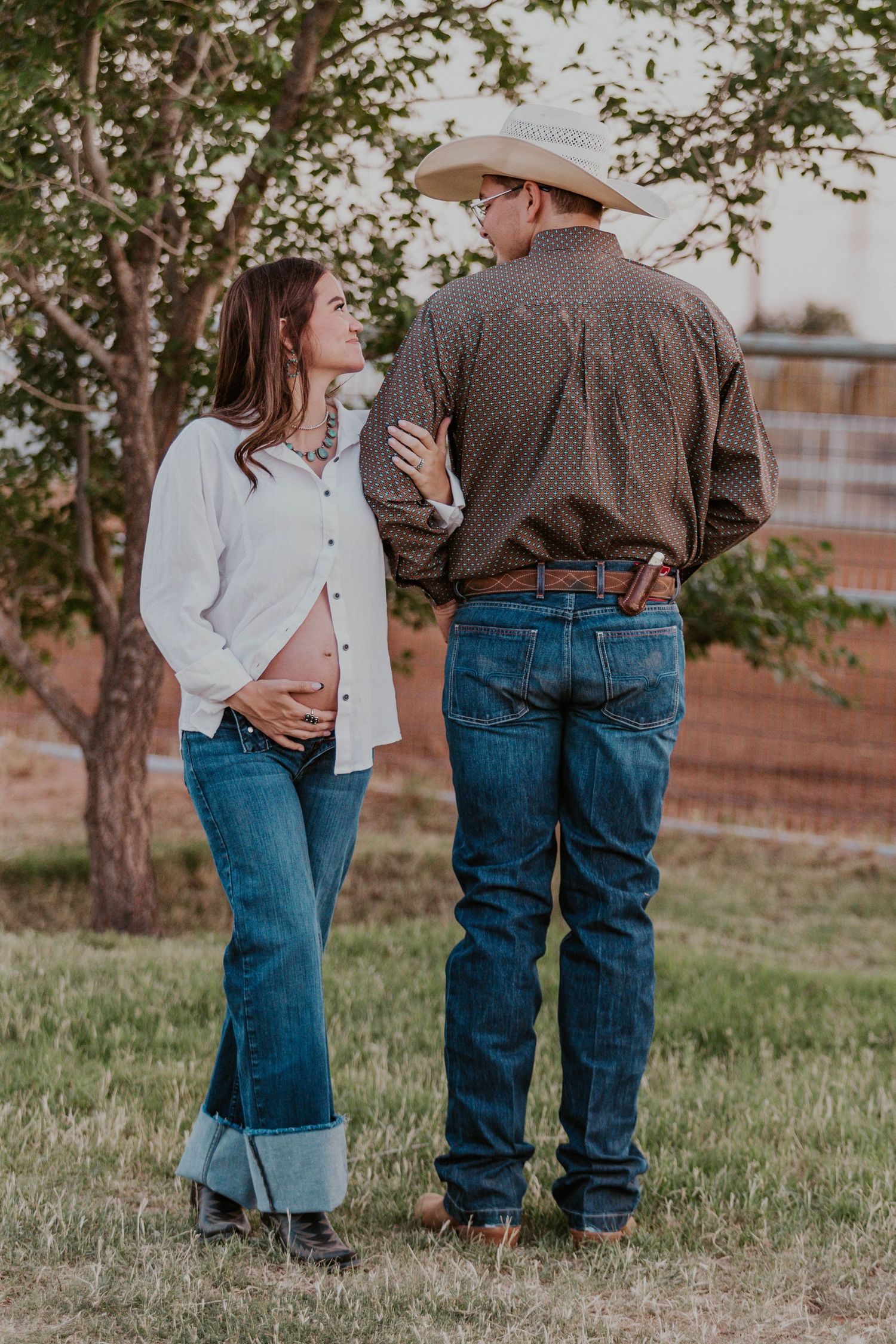 Expecting mom holds her belly at looks up at husband who has his back turned away.