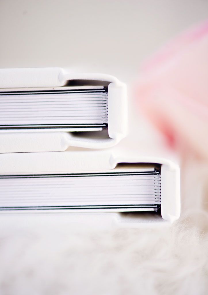 Close-up view of several white hardcover books stacked against a blurred pink background.
