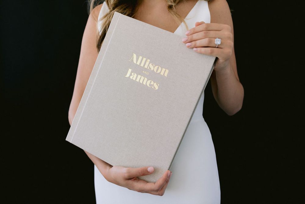 Gray leather wedding album with gold text held against white fabric.