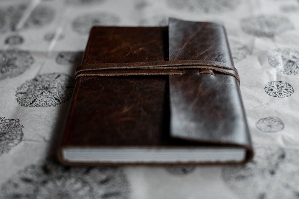 Vintage leather-bound book photographed on textured surface with delicate pattern details.