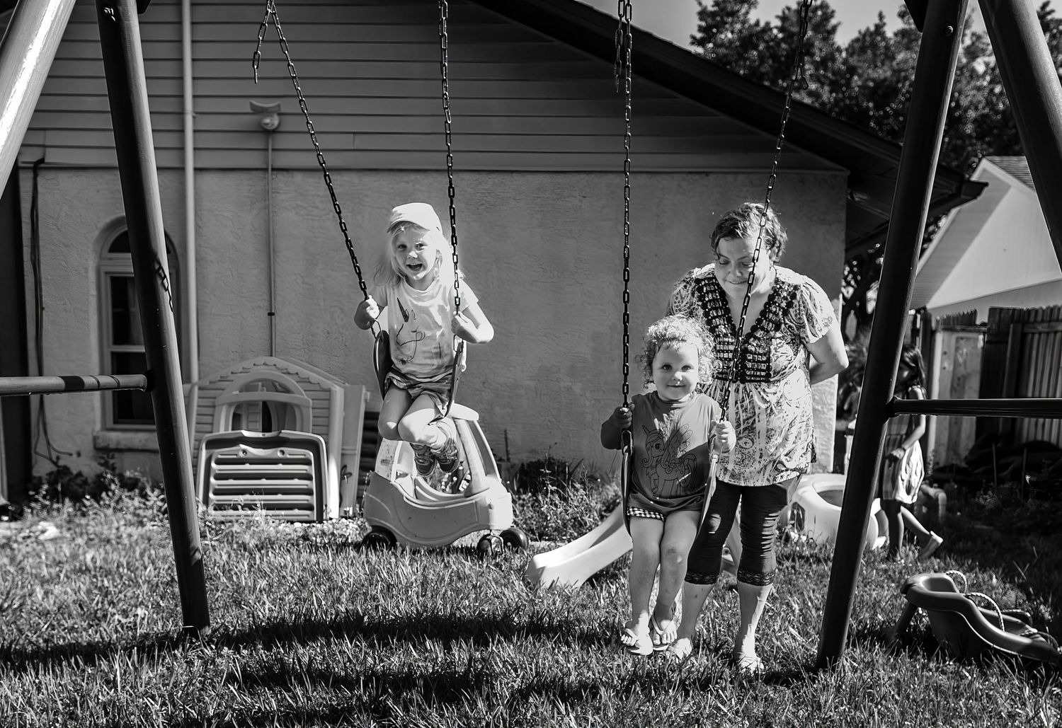 Black and white photograph of children playing on a backyard swing set in the summertime.