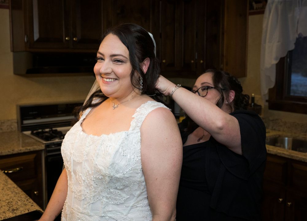 A bride in a white lace wedding dress smiles while getting ready in a bridal suite.
