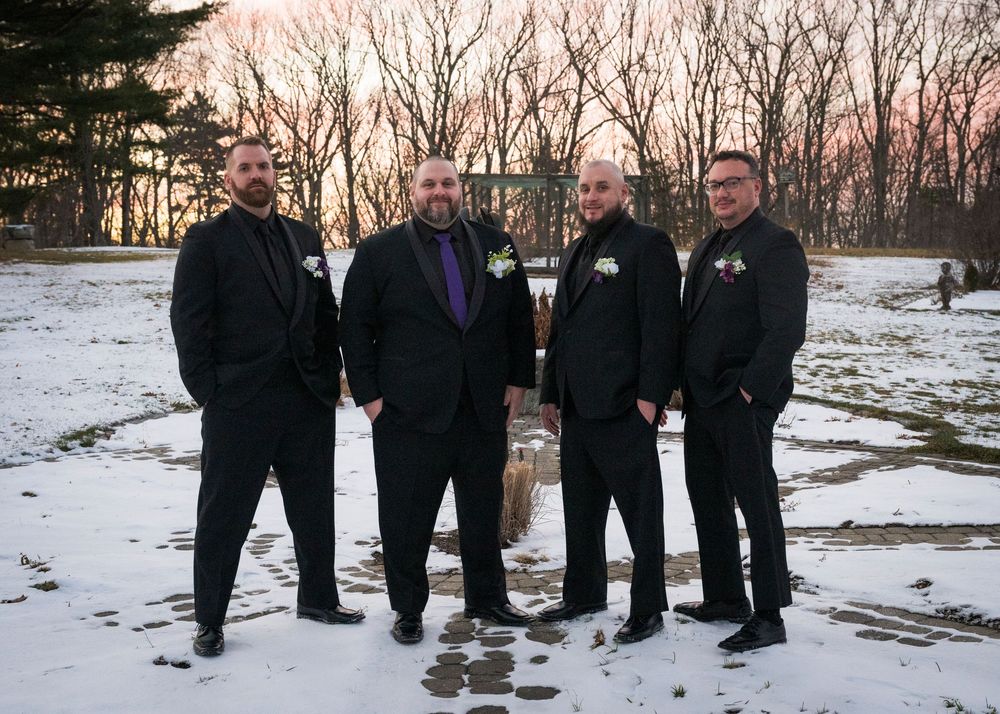 A group of people wearing dark winter coats stand together in a snowy landscape at dusk.