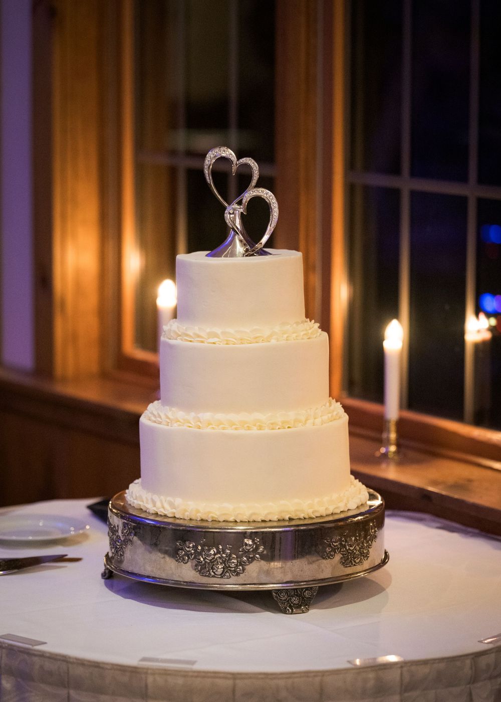 A classic white tiered wedding cake with delicate piping details displayed on an elegant silver platter.