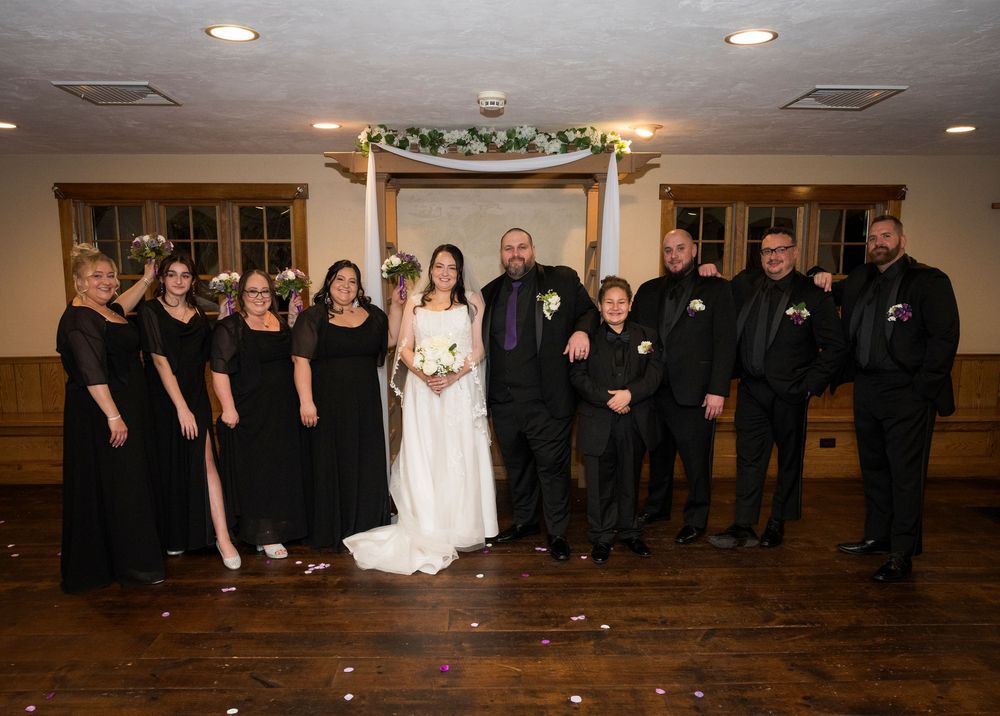 Wedding party lined up in a row wearing formal black and white attire in a reception venue.