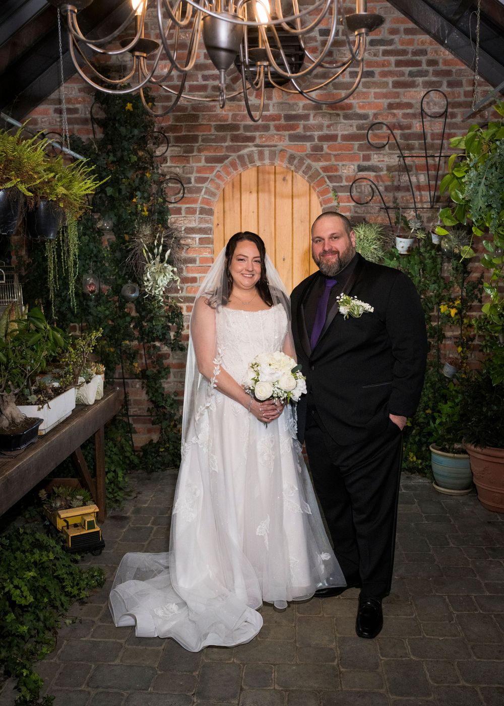 A couple poses together in an intimate courtyard setting with brick walls and romantic lighting for wedding photos.