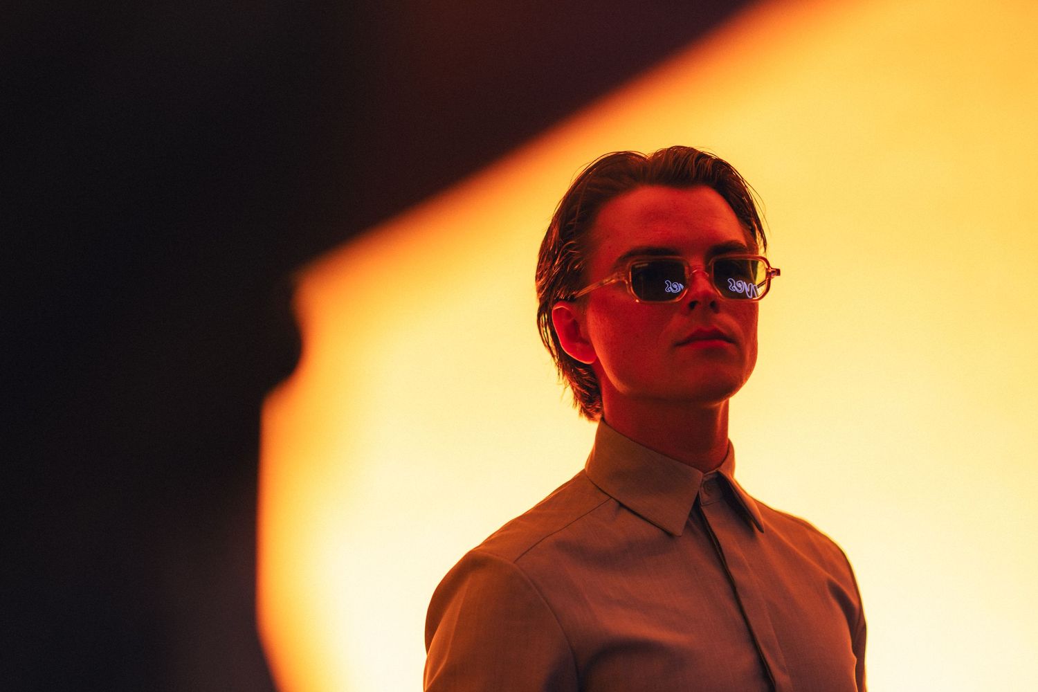 A cinematic silhouette scene with sunset-like orange lighting and figure wearing sunglasses in dramatic shadows.