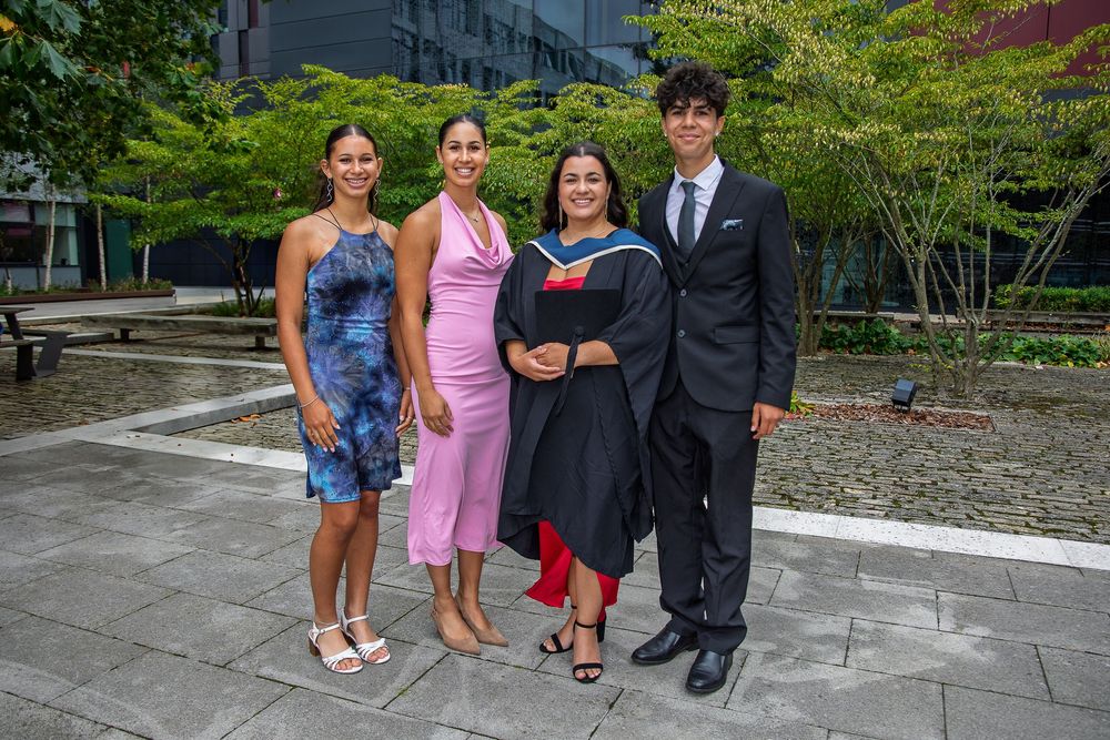 Group photo of graduates and family members posing together on stone patio surrounded by greenery.