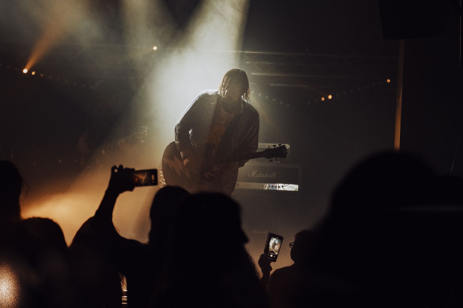 Silhouetted concert crowd and stage lighting create atmospheric performance scene.