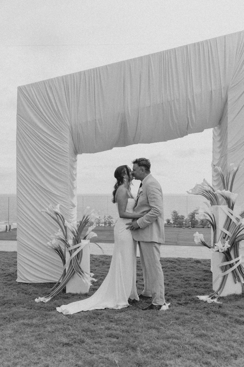 A black and white photo sequence showing a couple in wedding attire emerging from behind a draped white fabric backdrop.