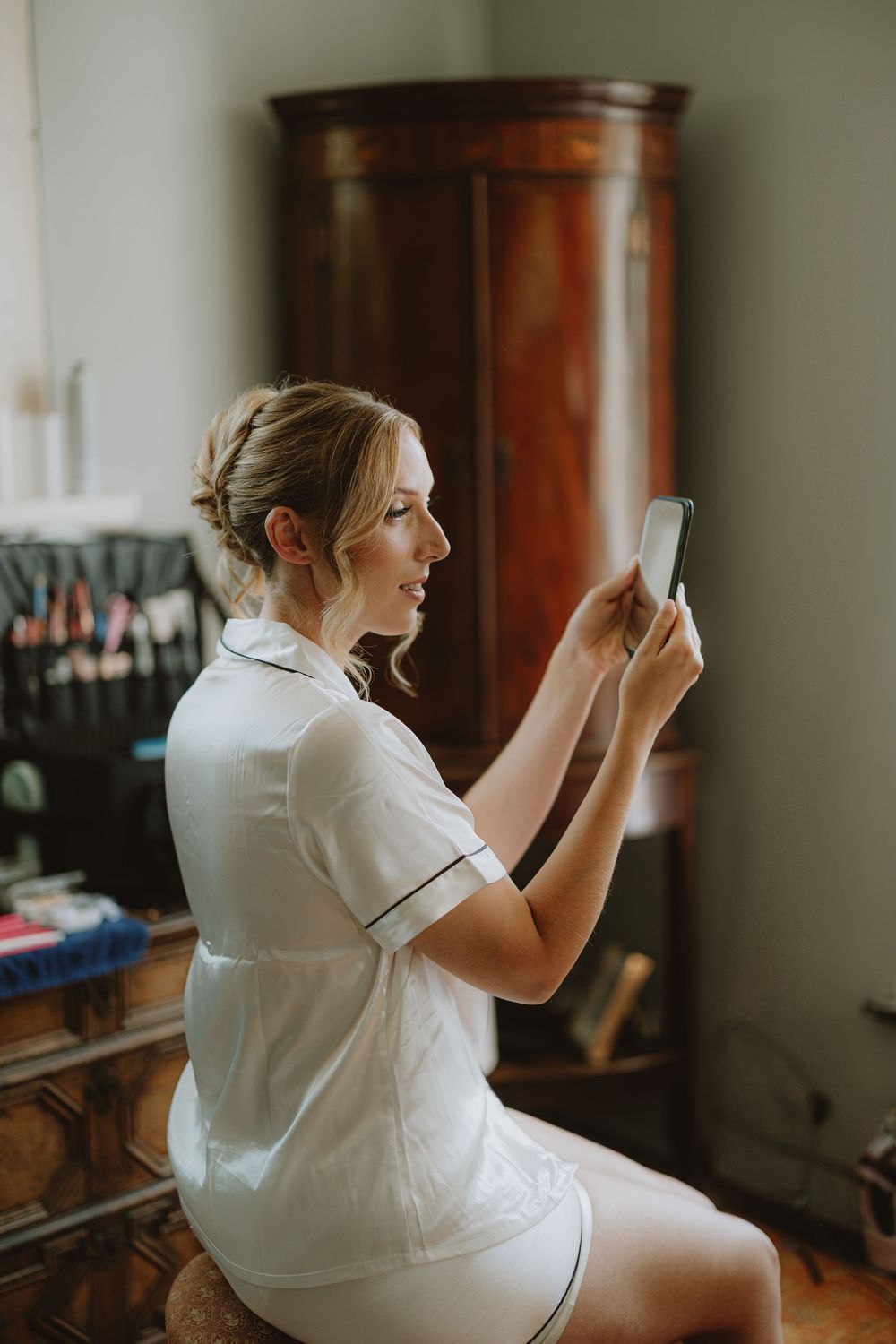 A person in white uniform checks their phone while sitting indoors near a wooden wardrobe.