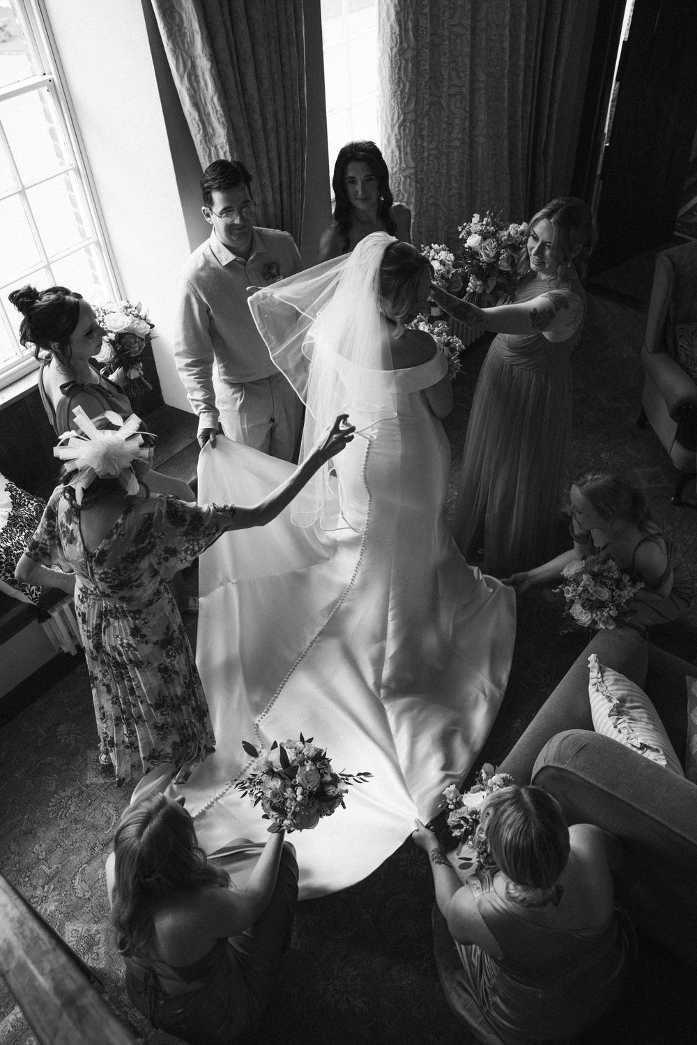 Wedding preparation scene with bridesmaids helping the bride get ready in natural window light.