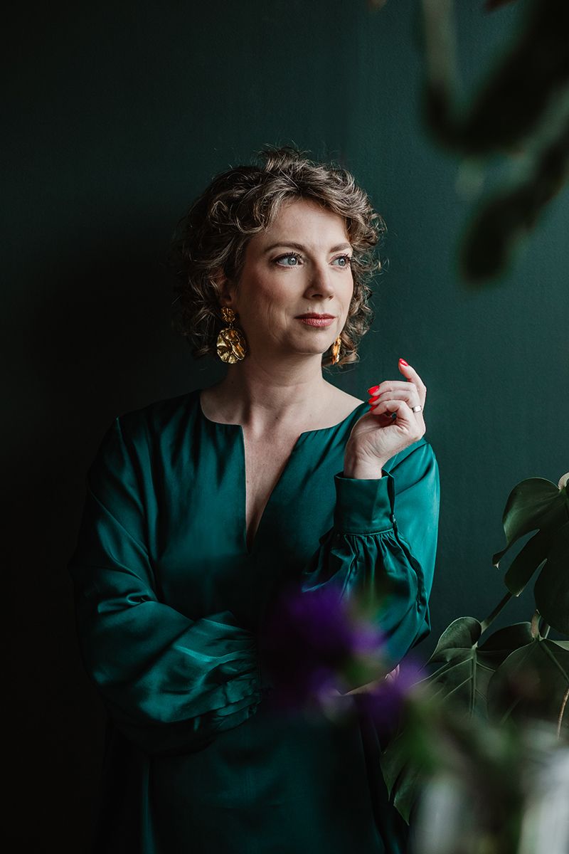 Vrouwelijke ondernemer met groene achtergrond en groene jurk kijkt naar buiten en het natuurlijke licht valt mooi op haar gezicht.