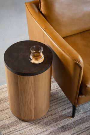 A series of modern cylindrical wooden side tables with black tops positioned next to a tan leather armchair.