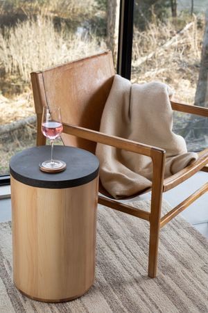 Modern living room scene with a tan leather lounge chair and round wooden accent table with wine glass on top.