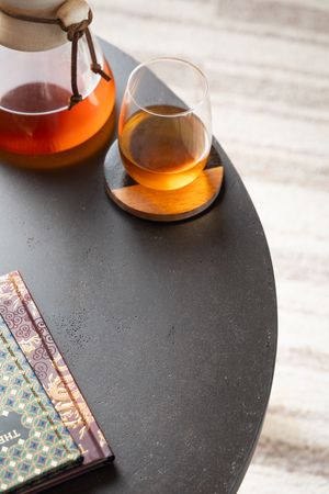 A glass of amber tea or brandy sits on a black slate surface next to colorful book spines.