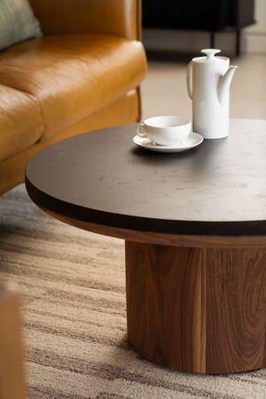 Modern coffee table features a round concrete top with a solid walnut wooden base and white coffee cups for styling.