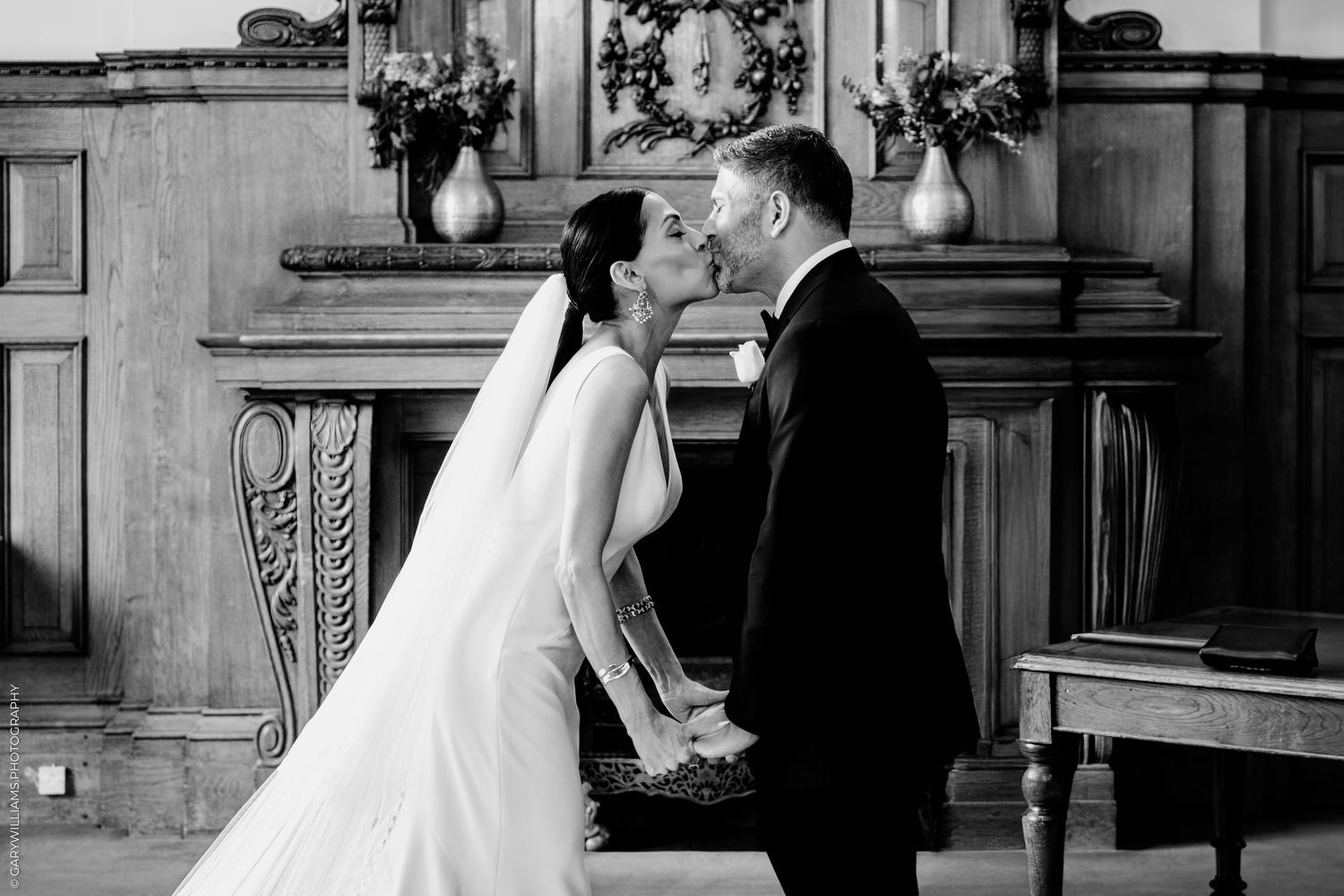 A couple shares a tender moment in black and white during their wedding ceremony in front of an ornate wooden altar.