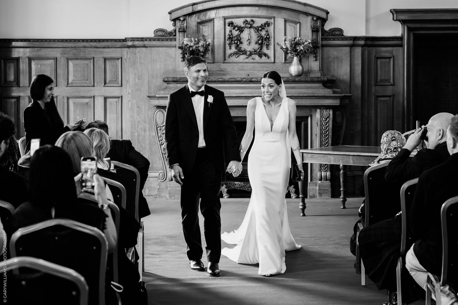 Wedding guests walk through an elegant hallway with classical wood paneling and decorative moldings during a ceremony.