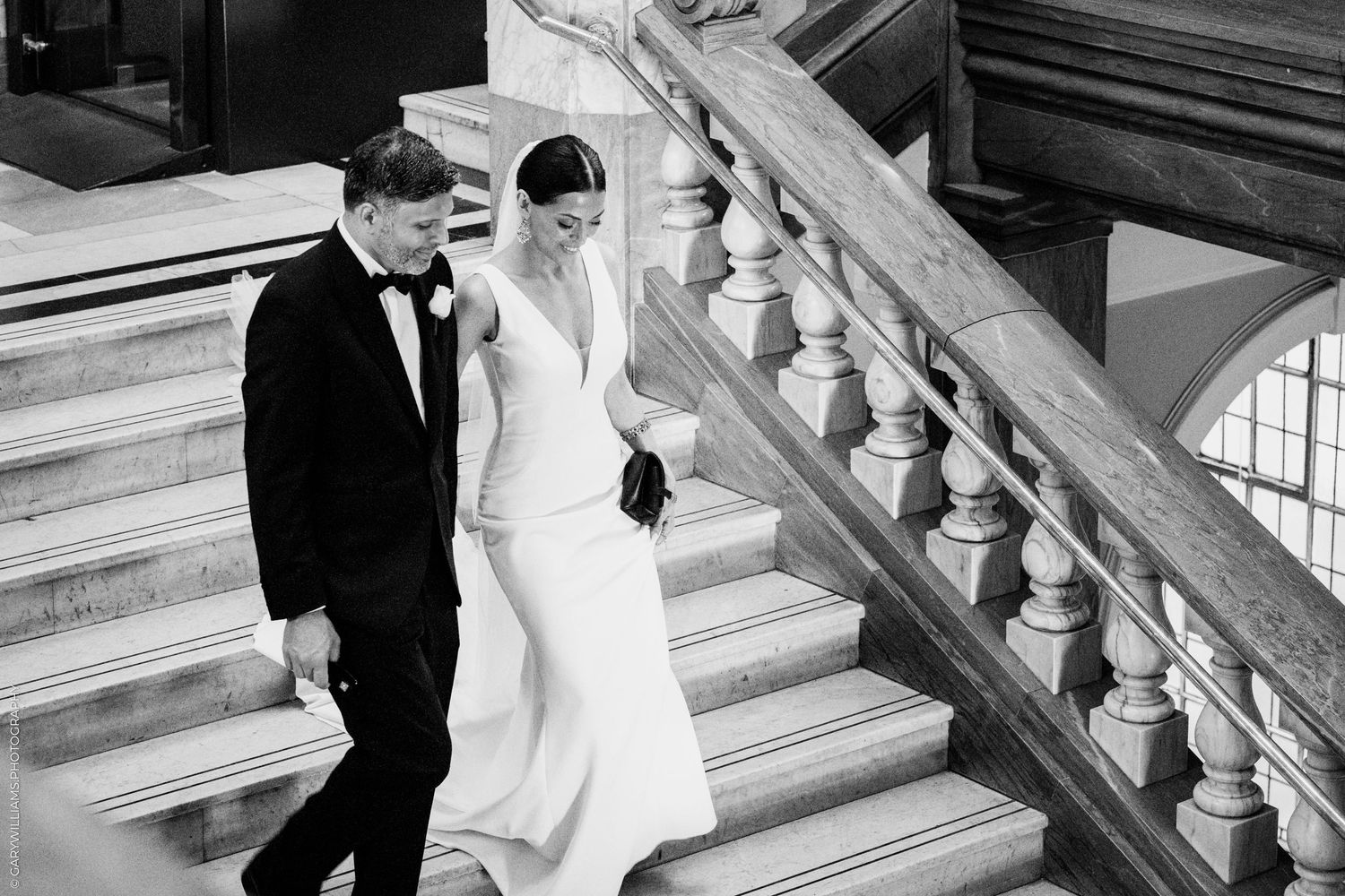 A bride and groom descend an elegant marble staircase together in black and white wedding photography.