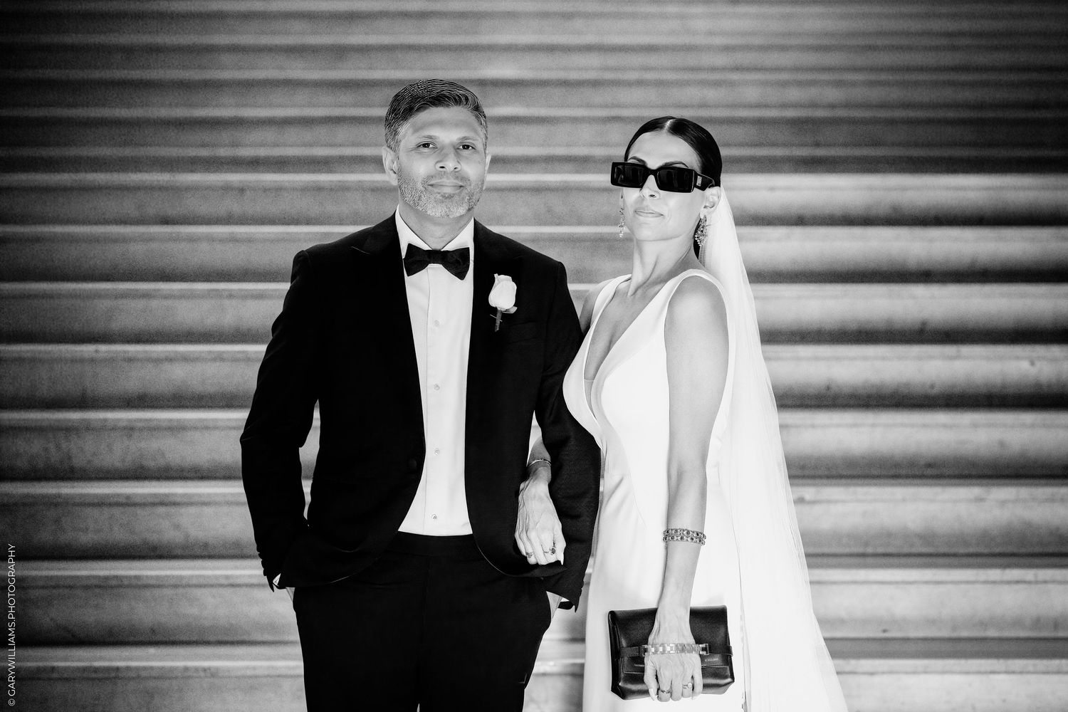 Black and white wedding photo showing bride and groom seated together on stone steps outdoors.
