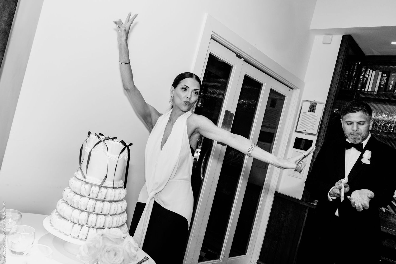 Black and white photo of a celebratory moment at a wedding reception with a large tiered white cake.