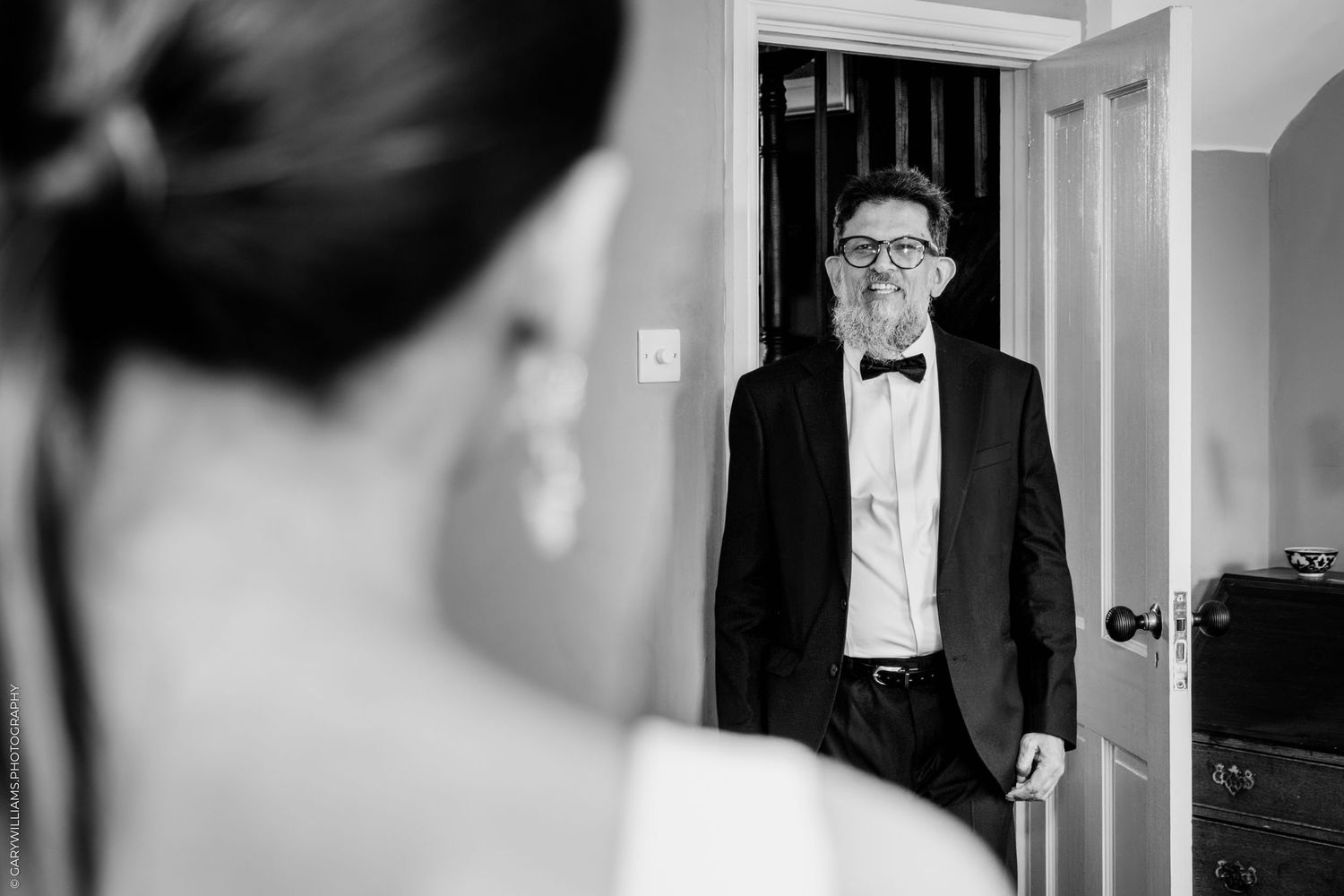 A touching first look moment between a groom in black tie and bow tie standing in a doorway.