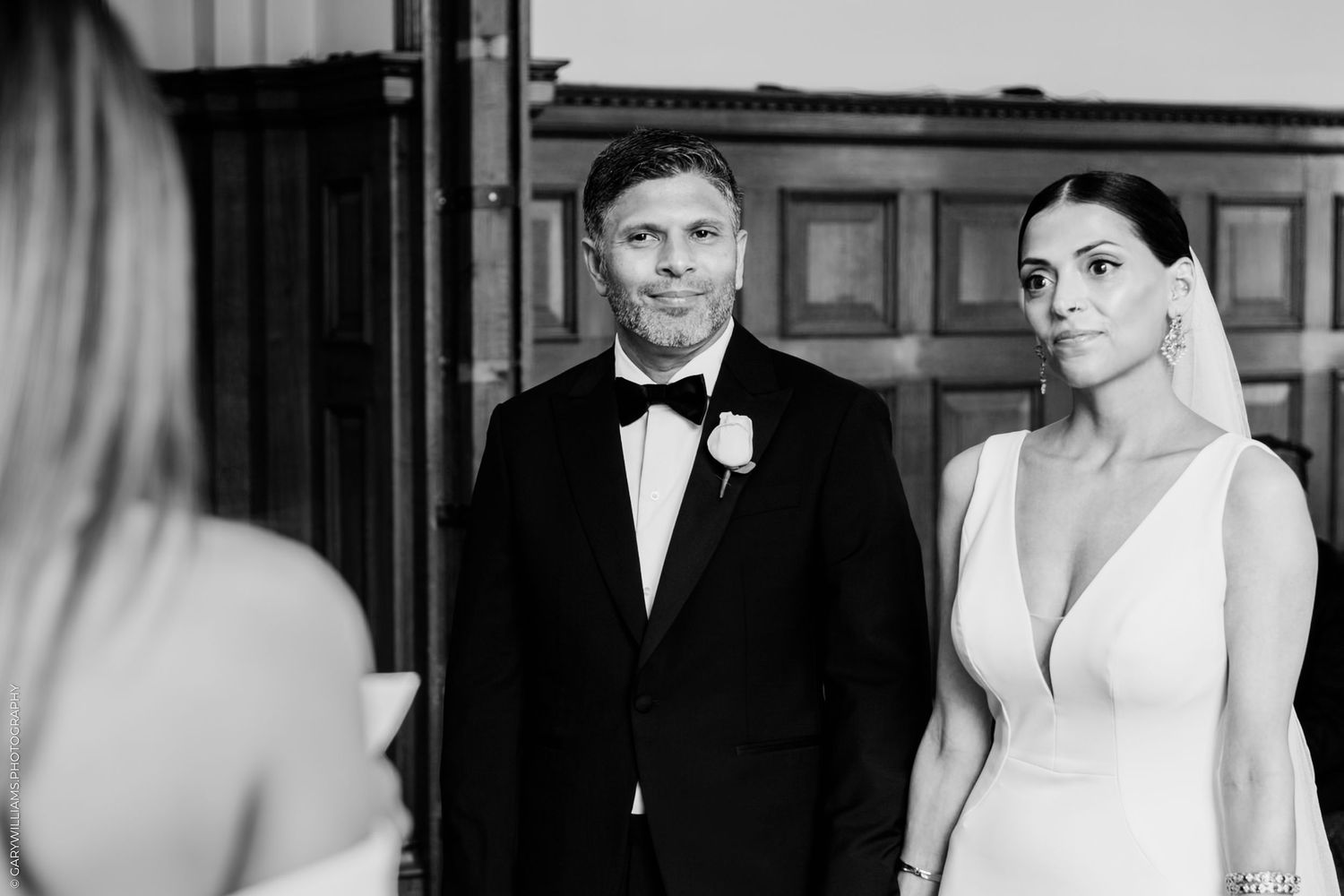 Black and white photograph showing a formal wedding couple embracing in an elegant interior setting.