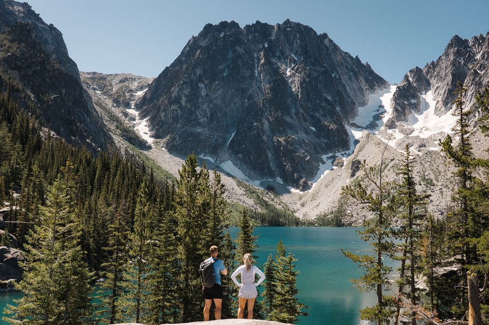Scenic mountain landscape with turquoise alpine lake surrounded by evergreen forest and snow-capped peaks in summer.
