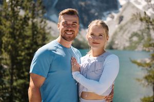 Two happy people smile together by a serene mountain lake on a summer day.