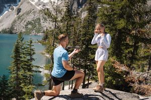 Couple hiking along mountain trail overlooking turquoise alpine lake and evergreen trees in scenic landscape.