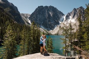 Hikers explore the scenic trail along Colchuck Lake with dramatic mountain peaks and evergreen forest in Washington state.
