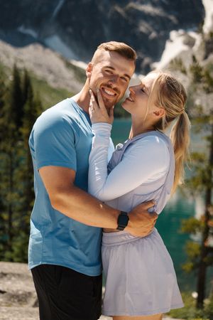 A couple shares romantic laughter and embraces near a scenic mountain lake on a sunny day. Colchuck Lake proposal