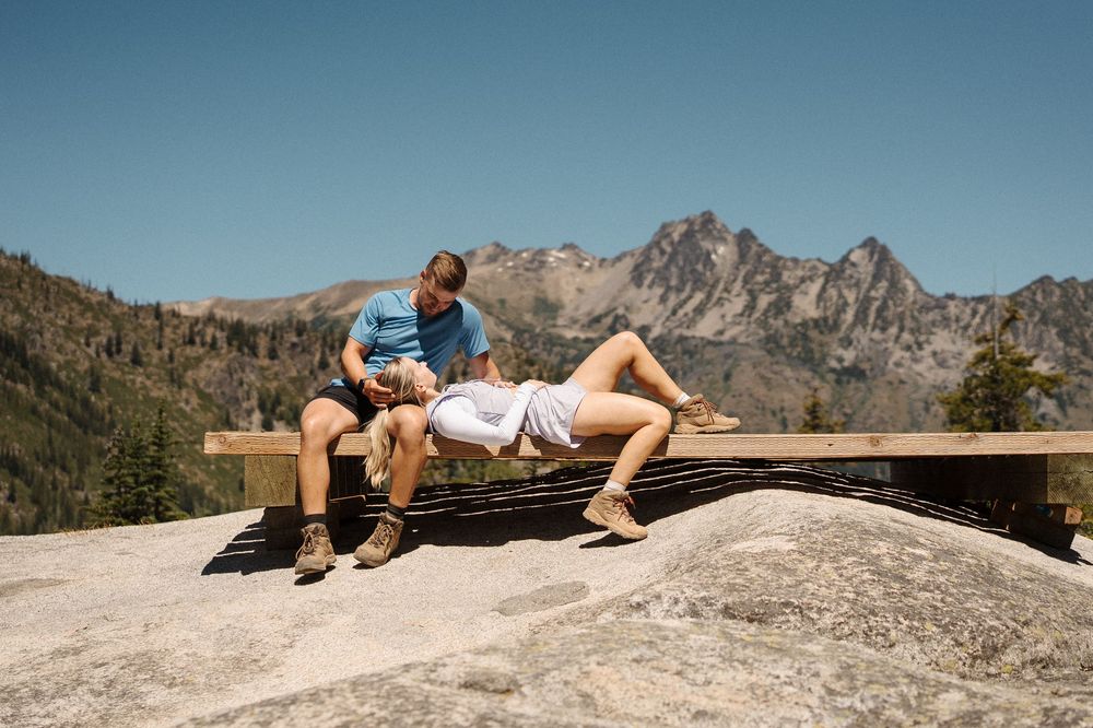 Someone relaxes on a scenic mountain summit while enjoying panoramic views of rugged peaks in the distance.