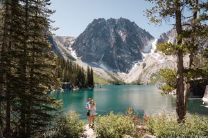 A stunning panoramic view of Colchuck Lake in Washington with turquoise waters surrounded by snow-capped mountains.