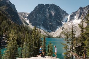 A turquoise alpine lake nestled between rocky mountain peaks and evergreen forest in the wilderness.