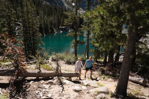 Hiker overlooking turquoise alpine lake surrounded by evergreen forest and rocky mountains in summer wilderness. Colchuck Lake proposal