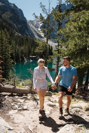 A couple hikes along a mountain trail overlooking a turquoise alpine lake surrounded by evergreen forest and peaks. Colchuck Lake proposal