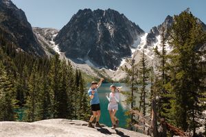 Two people enjoy a stunning view of Colchuck Lake proposal surrounded by snow-capped peaks in the Cascade Mountains.