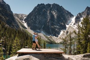 A hiker stands on a wooden platform overlooking Colchuck Lake proposal surrounded by snow-capped mountains in Washington state.