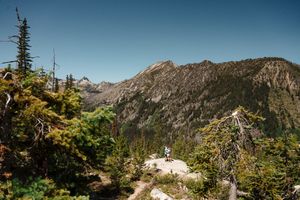 A panoramic view of rugged mountain peaks and evergreen trees in the wilderness on a clear sunny day. Colchuck Lake proposal