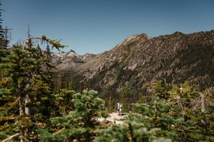 Rugged mountain peaks rise above evergreen forests in North Cascades National Park on a clear summer day. Colchuck Lake proposal