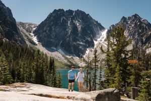 Two people admire Colchuck Lake surrounded by snow-capped peaks and evergreen trees in the Cascade Mountains. Colchuck Lake proposal