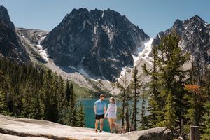 Two people standing on a rocky viewpoint overlooking Colchuck Lake and Dragontail Peak in the Cascade Mountains. Colchuck Lake proposal