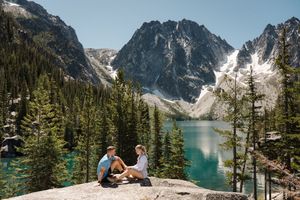 Stunning mountain lake vista with snow-capped peaks reflecting in turquoise waters surrounded by evergreen forest Colchuck Lake proposal